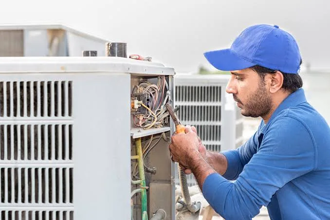 Technician repairing wiring inside an outdoor HVAC unit